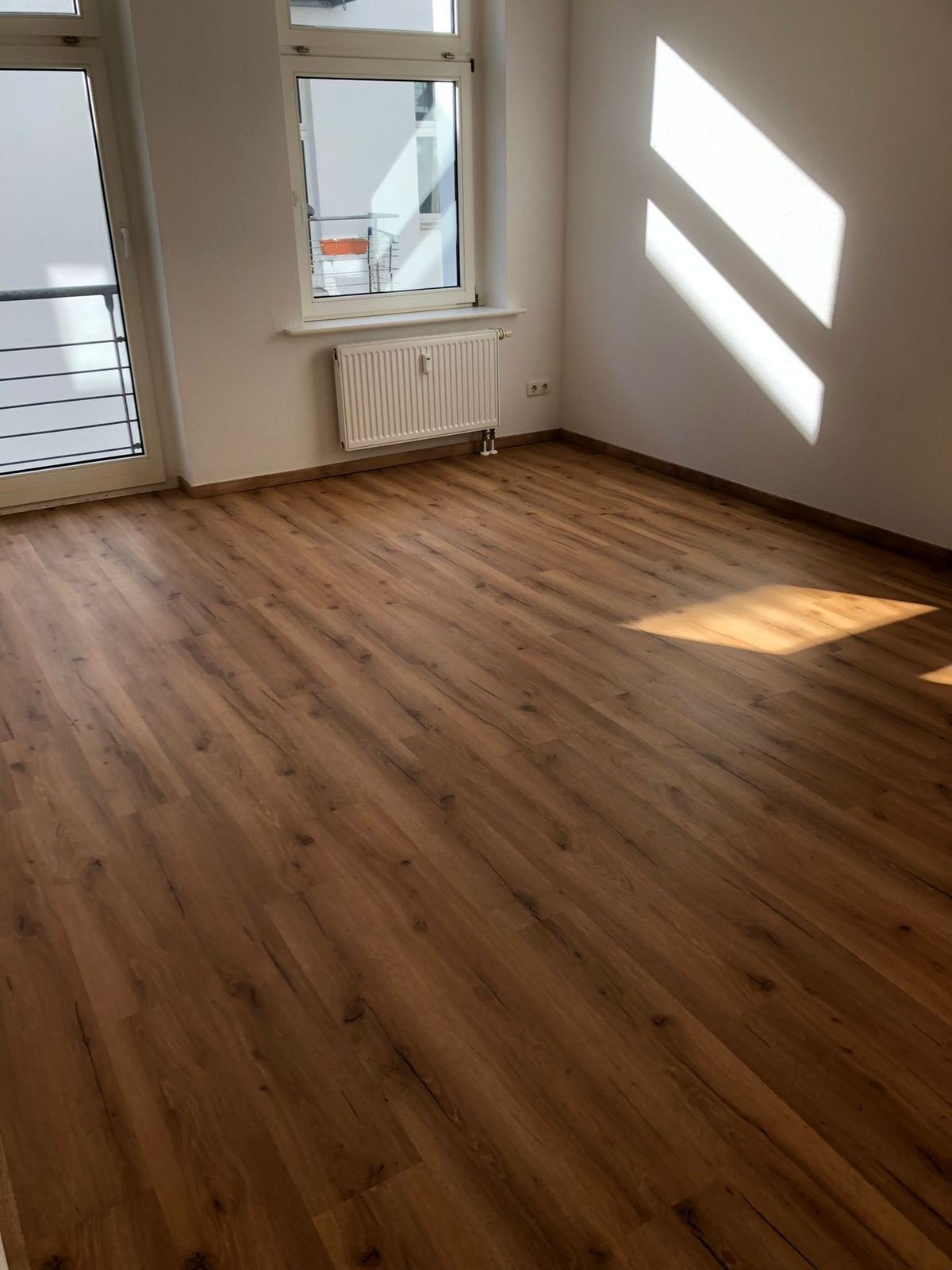 Renoviertes Zimmer einer Altbauwohnung in Magdeburg mit neuem Boden in Holzoptik und weißen Wänden