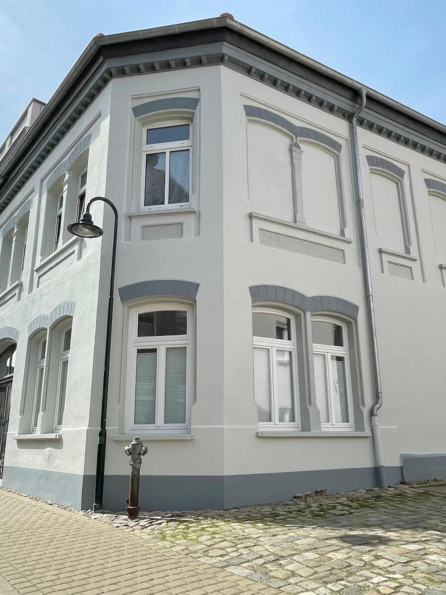 Nachher: frisch sanierte Altbaufassade mit hellem Anstrich und grauen Zierelementen